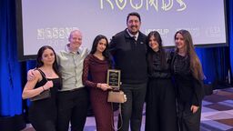 Students pose on stage holding a plaque